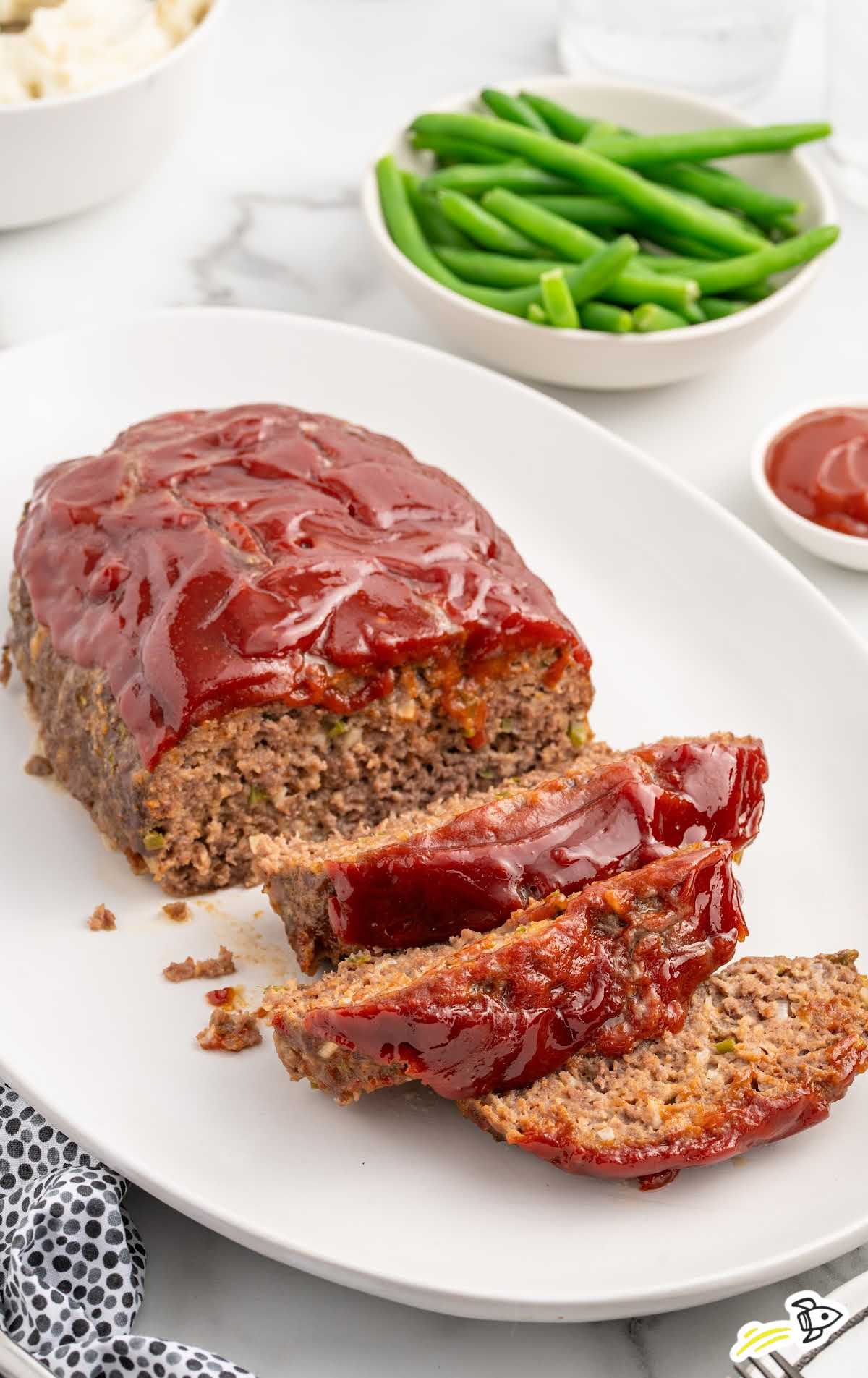 meatloaf on a serving tray with a bowl of green beans