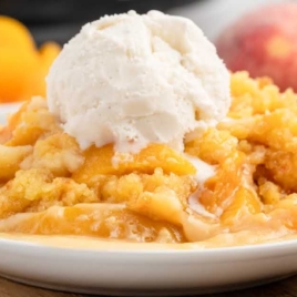 a serving of Peach Dump Cake topped with vanilla ice cream on a plate