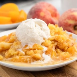 a serving of Peach Dump Cake topped with vanilla ice cream on a plate