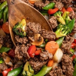 Ground beef stir fry with colorful vegetables being scooped with a wooden spoon.