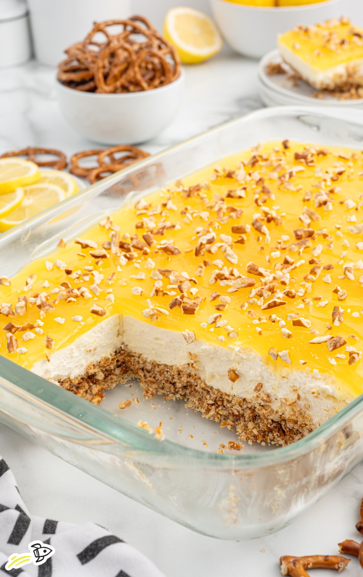 A glass pan of lemon pretzel salad with slices missing from it.