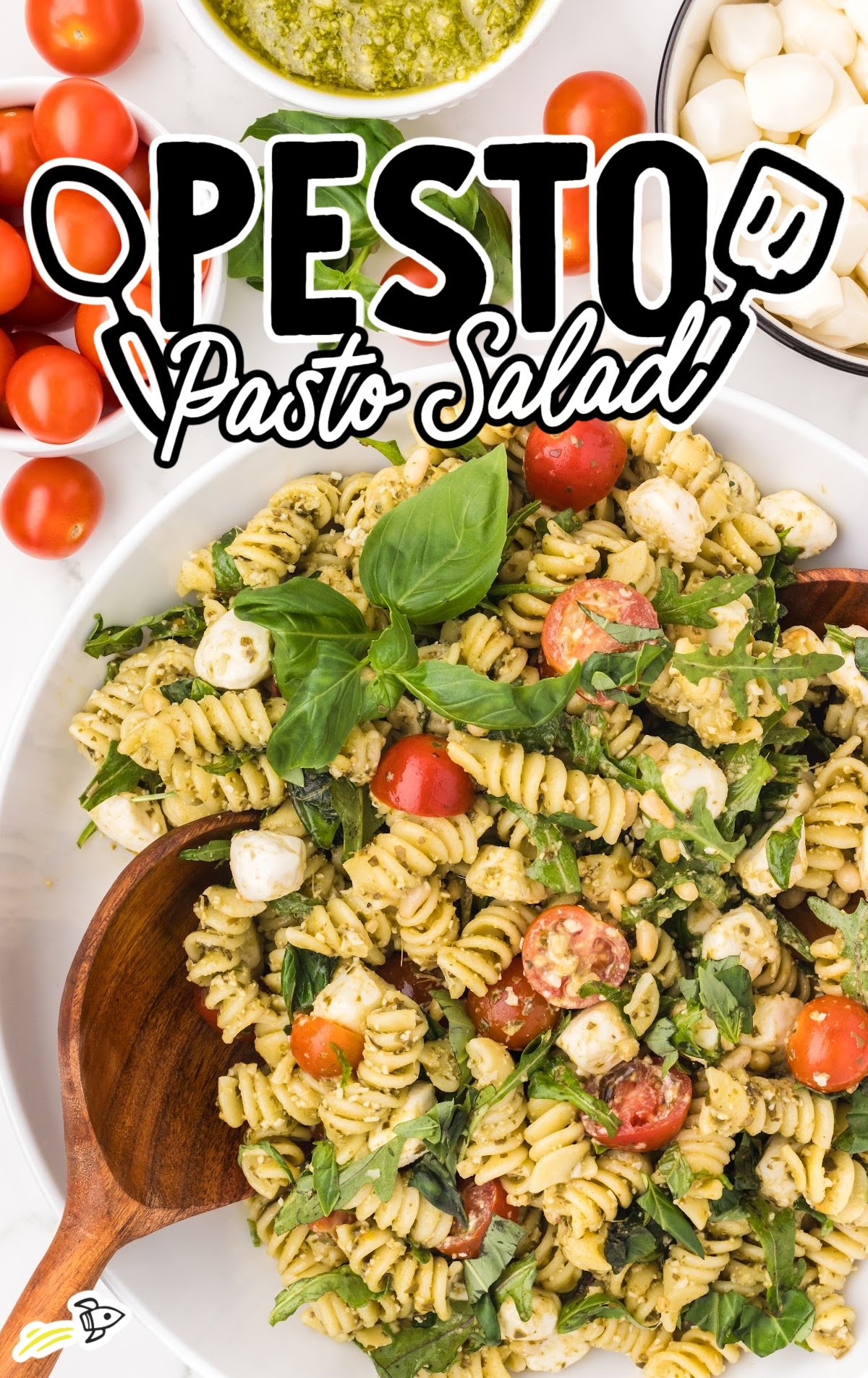 a bowl of Pesto Pasta Salad topped with basil with a large wooden spoon