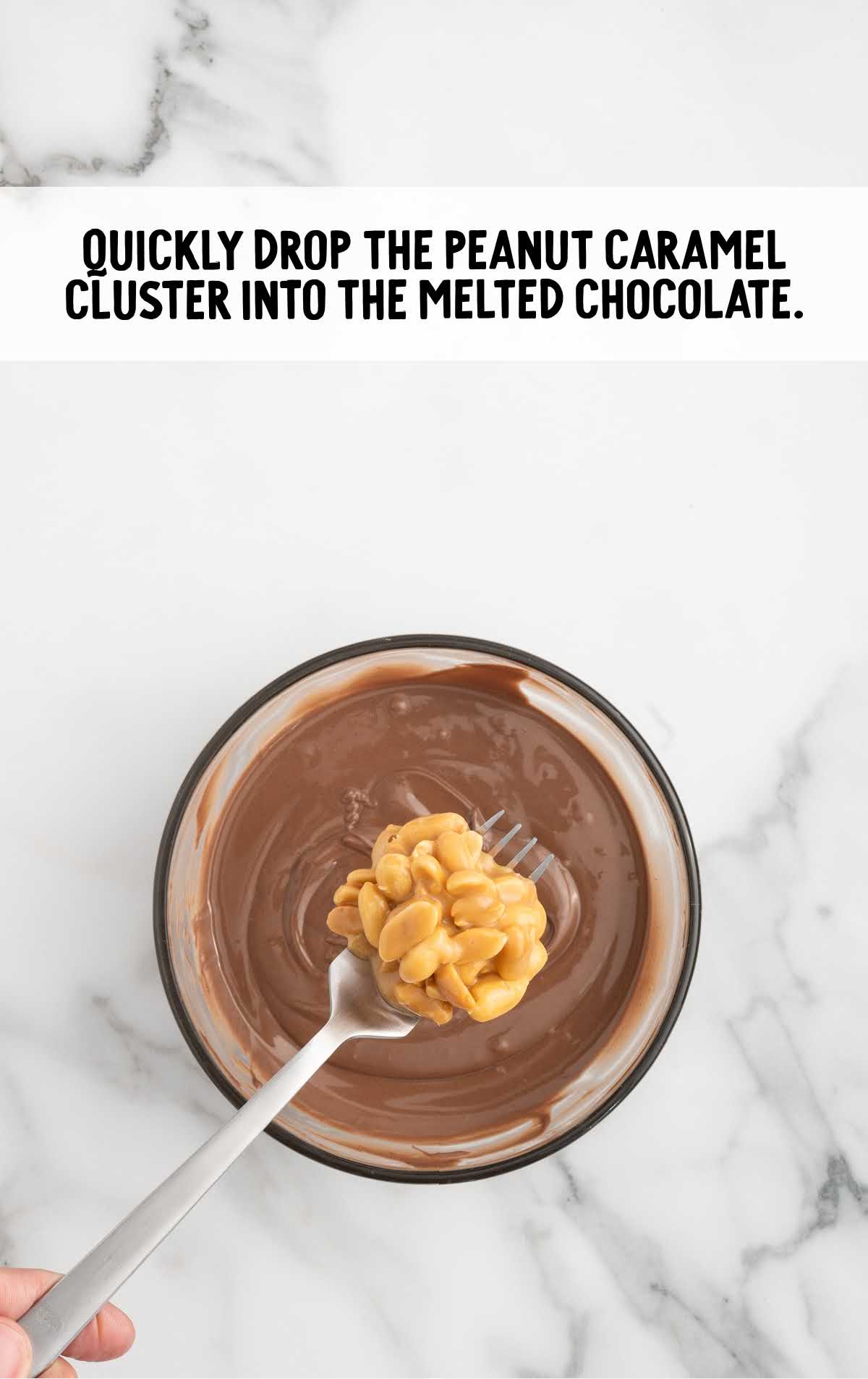 peanut caramel cluster dropped into the bowl of melted chocolate