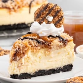 a slice of Samoa Cheesecake topped with whipped topping and samoa cookies on a plate