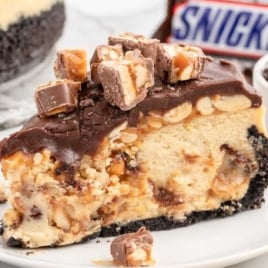 a slice of Snickers Cheesecake topped with crushed Snickers on a plate