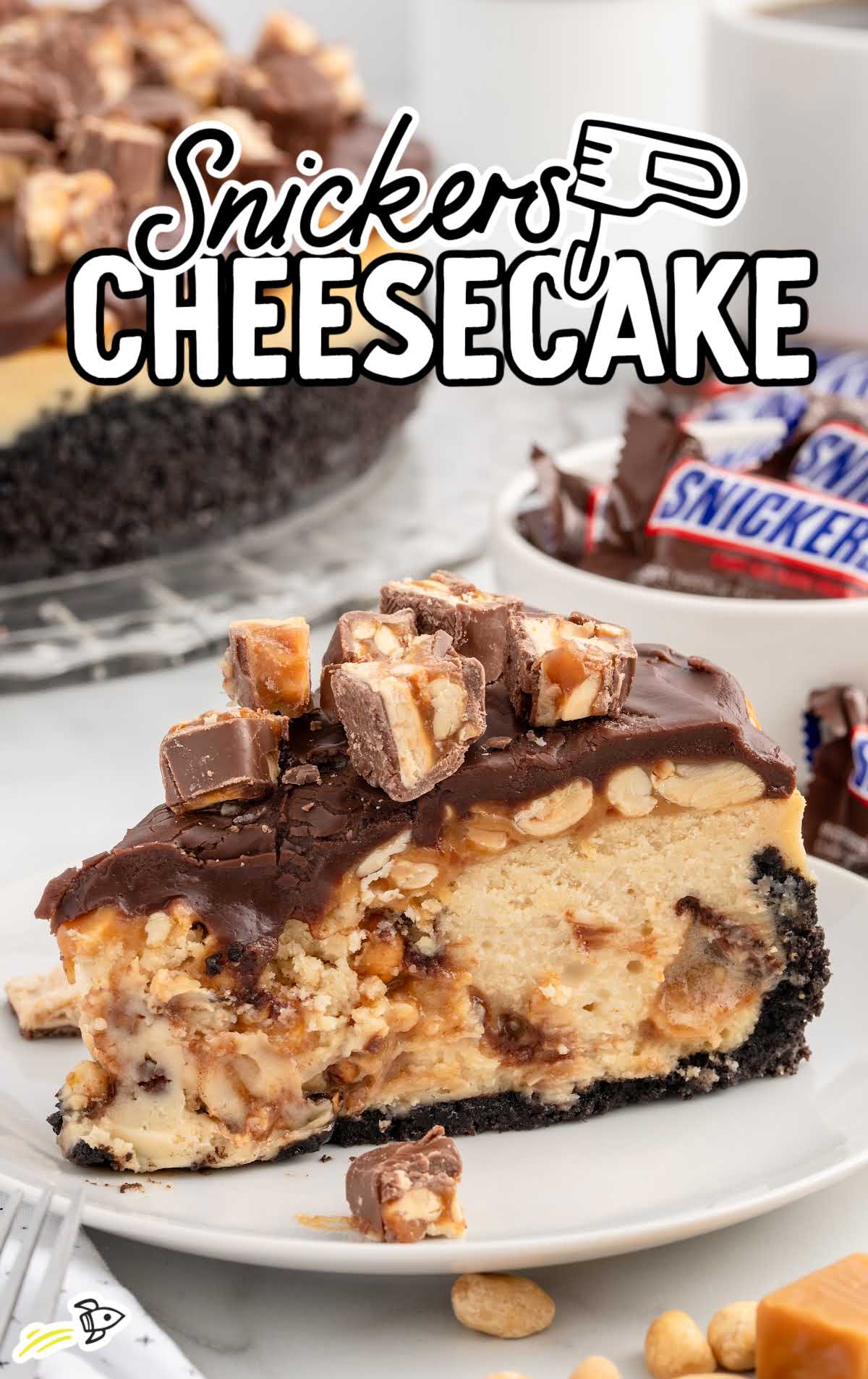 a slice of Snickers Cheesecake topped with crushed Snickers on a plate