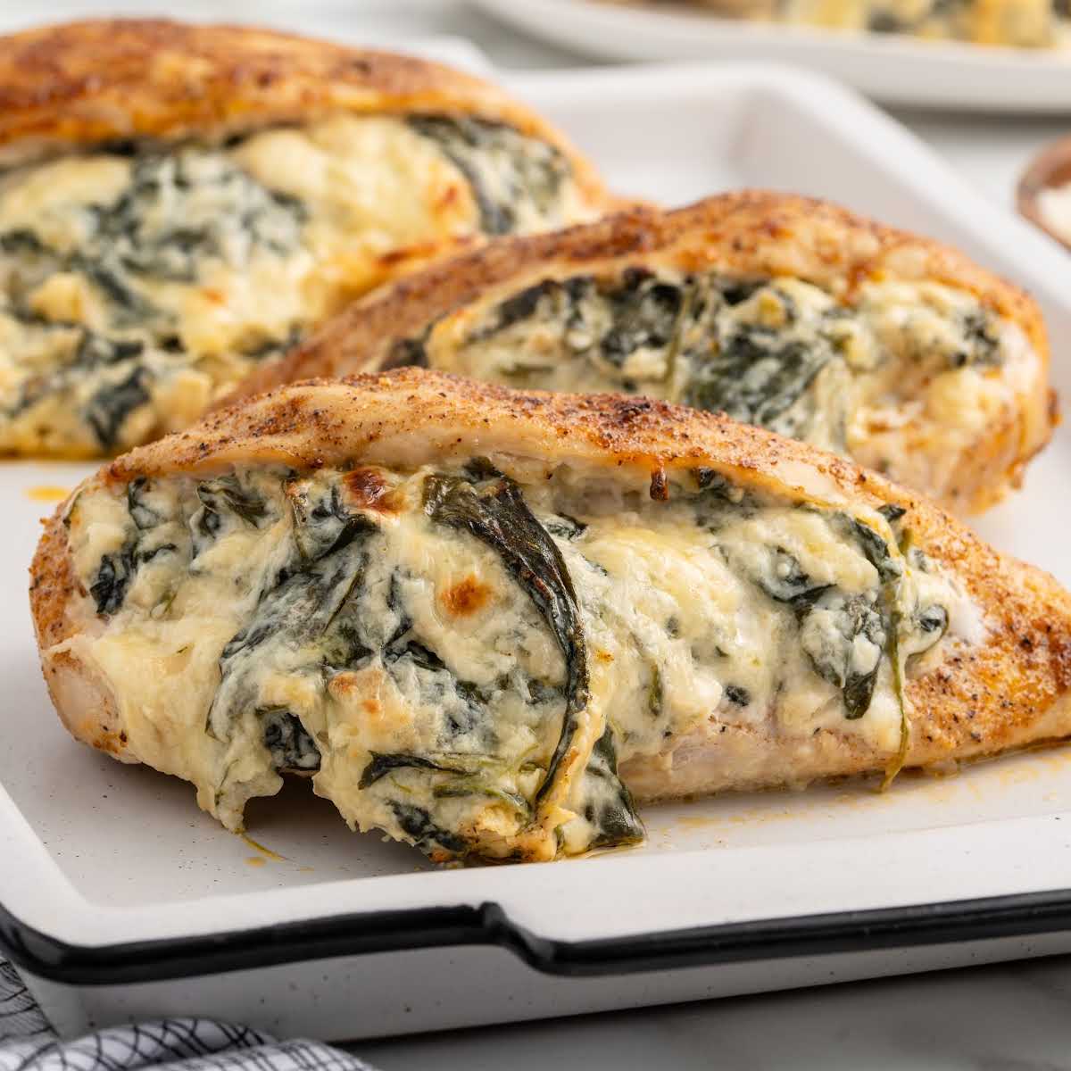 Three baked spinach stuffed chicken breasts on a tray.