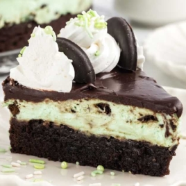 a slice of Thin Mint Cheesecake topped with whipped topping, thin mint cookies, and sprinkles on a plate