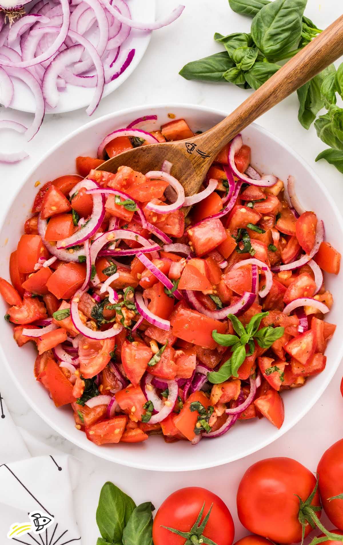 a bowl of Tomato and Onion Salad topped with basil and a large wooden spoon