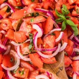 a bowl of Tomato and Onion Salad topped with basil and a large wooden spoon