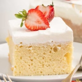 a slice of Tres Leches Cakes topped with a slice of strawberry on a plate