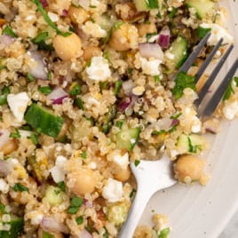 A plate of quinoa salad with chickpeas, cucumber, red onion, herbs, and feta cheese—this vibrant Jennifer Aniston Salad is a refreshing and satisfying meal. A fork rests on the plate. Text reads The Hollywood Salad: Jennifer Aniston Salad.