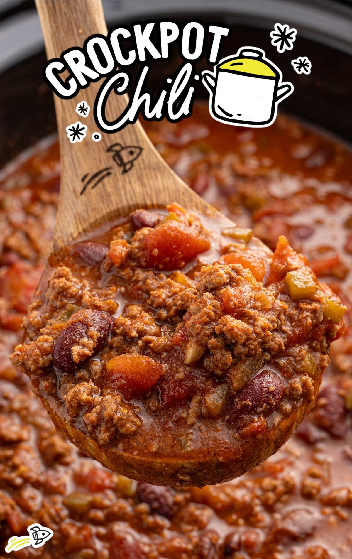 Wooden spoon scooping thick chili from crockpot, showing chunks of tomato, beef, beans, and peppers.
