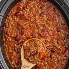 Overhead shot of crockpot chili with text overlay “Crockpot Chili – Easy Method, Perfect Every Time!” above a wooden spoon full of chili.