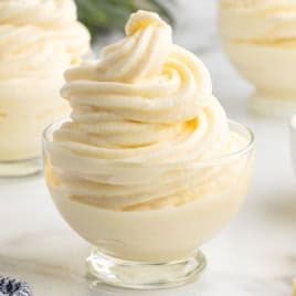 A glass dish filled with creamy, swirled pineapple soft serve, made from a classic Dole Whip Recipe, sits on a white surface with more dessert cups visible in the background.