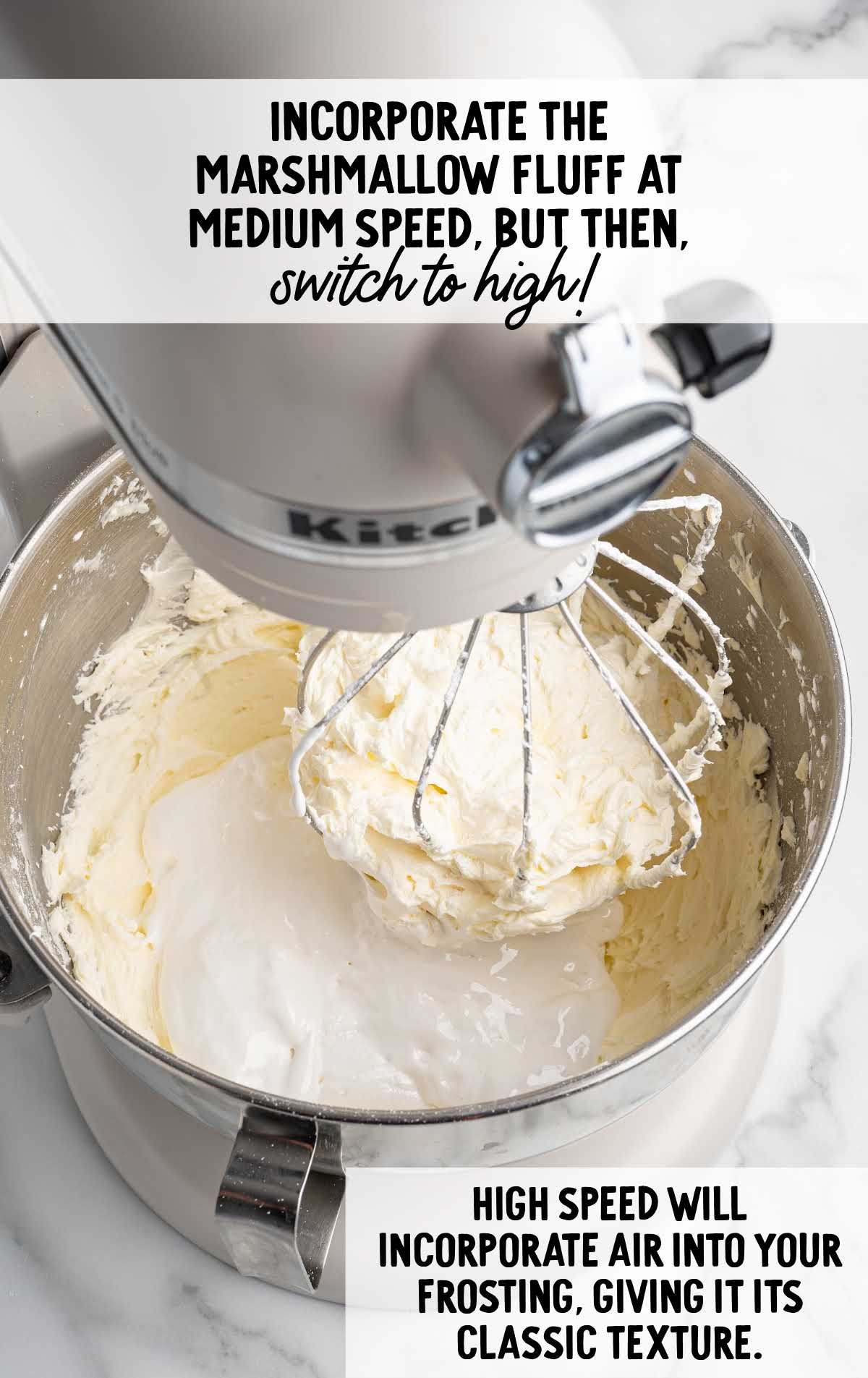 Mixer bowl with marshmallow fluff and frosting being whipped to incorporate air for fluffy texture