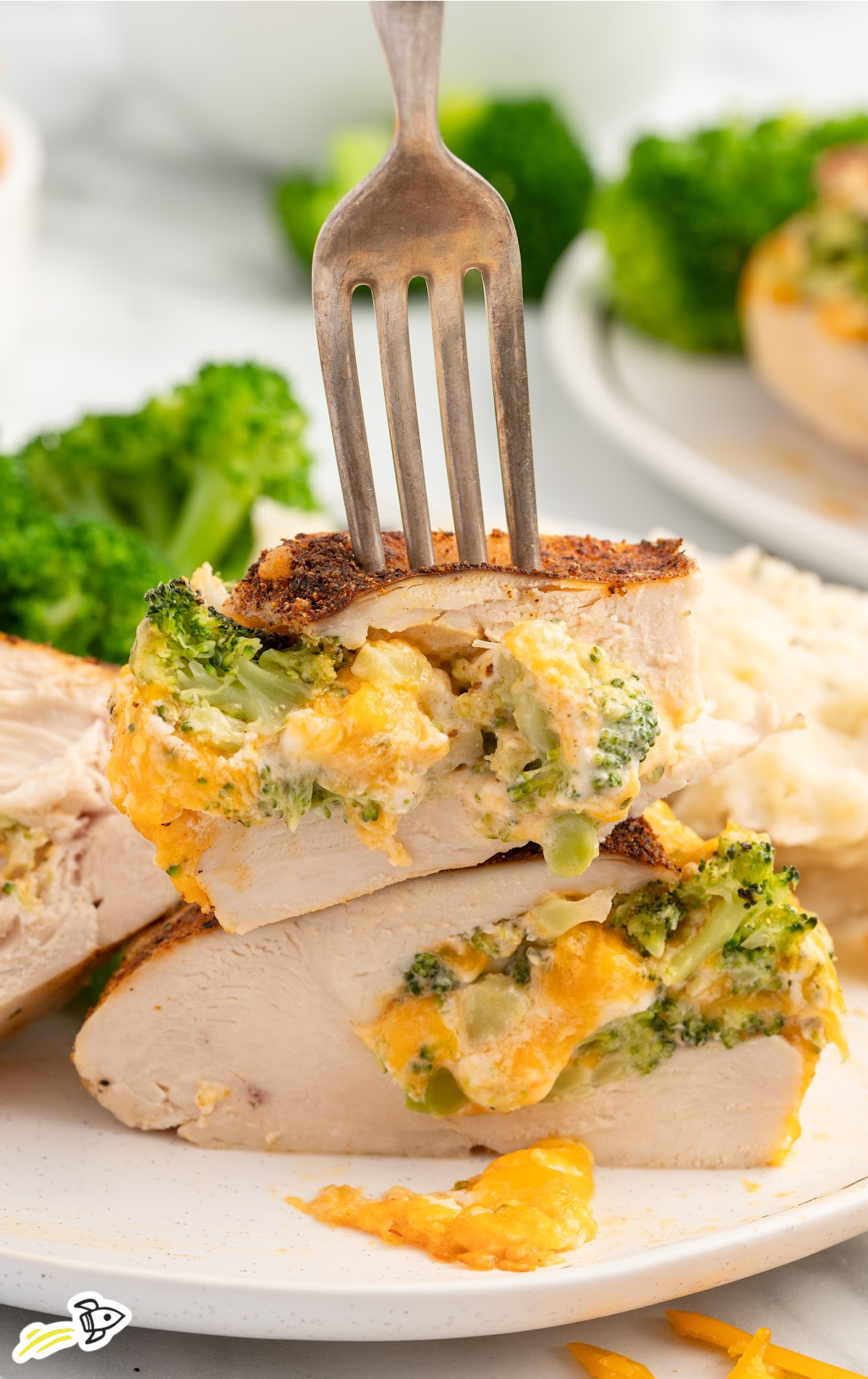 A piece of Broccoli and Cheese Stuffed Chicken Breast cut open with a fork lifting a bite of it.