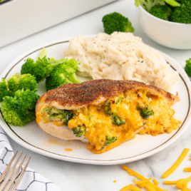 A white dinner plate contains a piece of Broccoli and Cheese Stuffed Chicken Breast and mashed potatoes with broccoli.