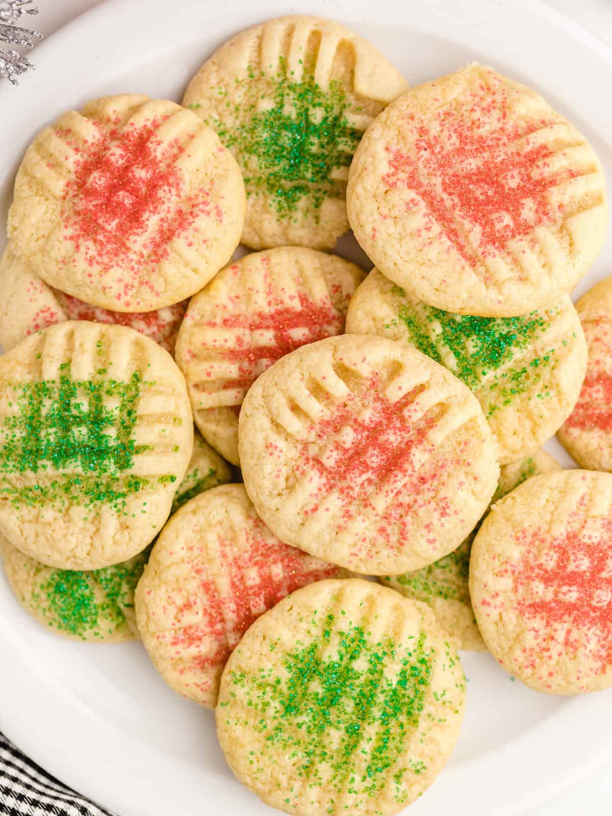 A plate of Christmas Sugar Cookies topped with red and green sugar sprinkles, each cookie marked with a crisscross fork pattern.