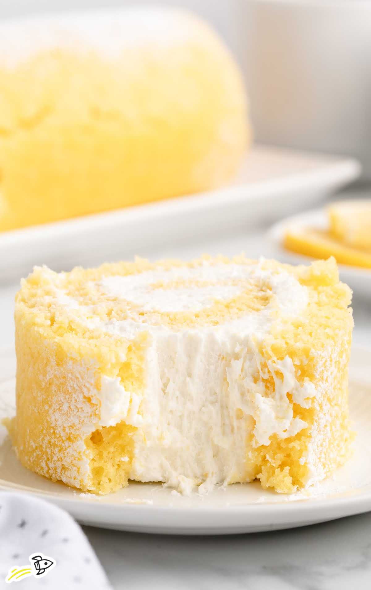 Bite taken out of lemon swiss roll slice showcasing soft cake and creamy filling