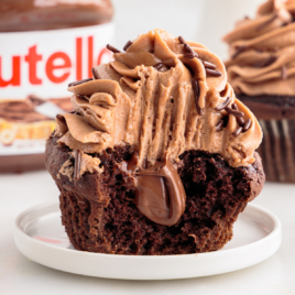 A nutella cupcake on a white plate with a big bite out of it, showing the nutella frosting filling.