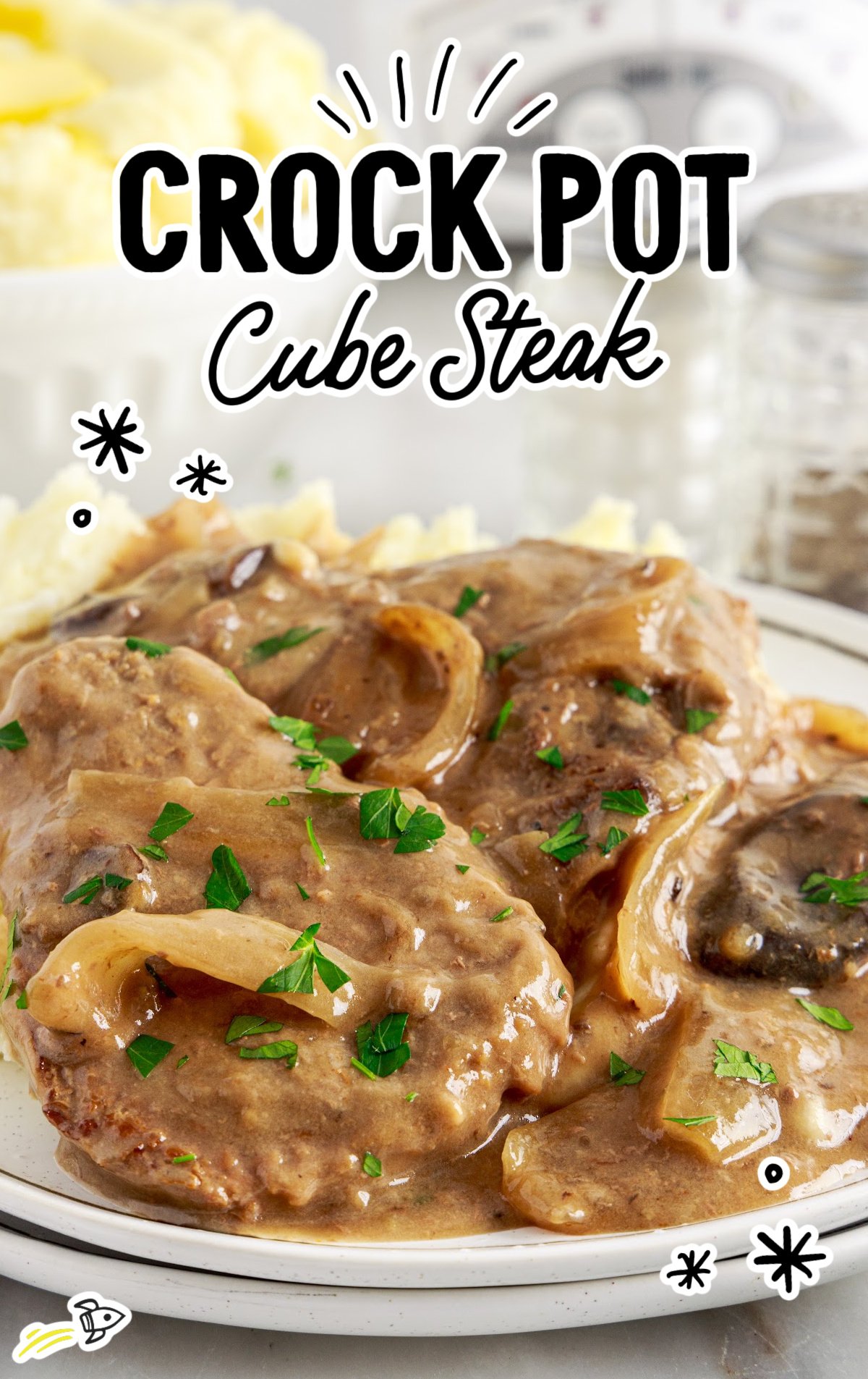 A white dinner plate of crock pot cube steak with gravy and onions. 