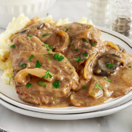 A dinner plate with crock pot cube steak covered i gravy with mashed potatoes.