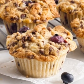 A Blueberry Chocolate Chip Muffin on a plate surrounded by more Blueberry Chocolate Chip Muffins.