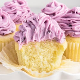 A cupcake topped with blueberry cream cheese frosting. it has a big bite out of it.