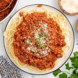 a plate of spaghetti with bolognese sauce garnished with parsley and topped with grated parmesan
