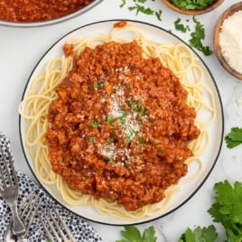 a plate of spaghetti with bolognese sauce garnished with parsley and topped with grated parmesan