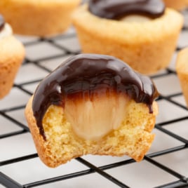 A wire rack covered in boston cream pie cookie cups. One has a bite out of it.