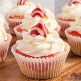 A bunch of candy cane cupcakes are on a serving board, garnished with buttercream and hershey kisses.