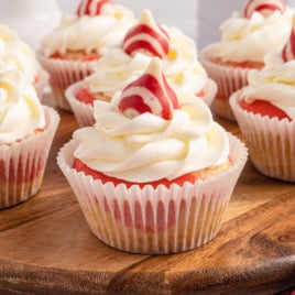 A bunch of Candy Cane Cupcakes on a wooden serving tray. They are garnished with buttercream and a hersheys peppermint kiss.