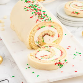 A slice of the Christmas Roll is cut off the end on a white serving platter.