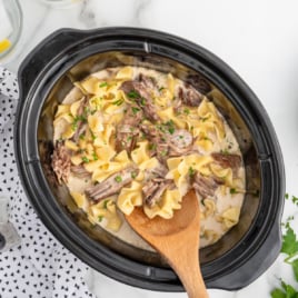 Crock Pot Beef and noodles in a slow cooker with a wooden spoon in it.