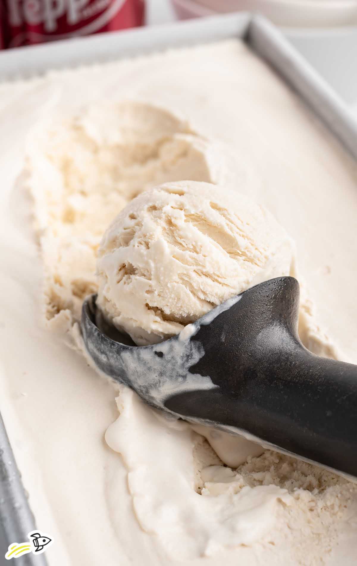 Scooping homemade Dr Pepper ice cream from a loaf pan with a black ice cream scoop