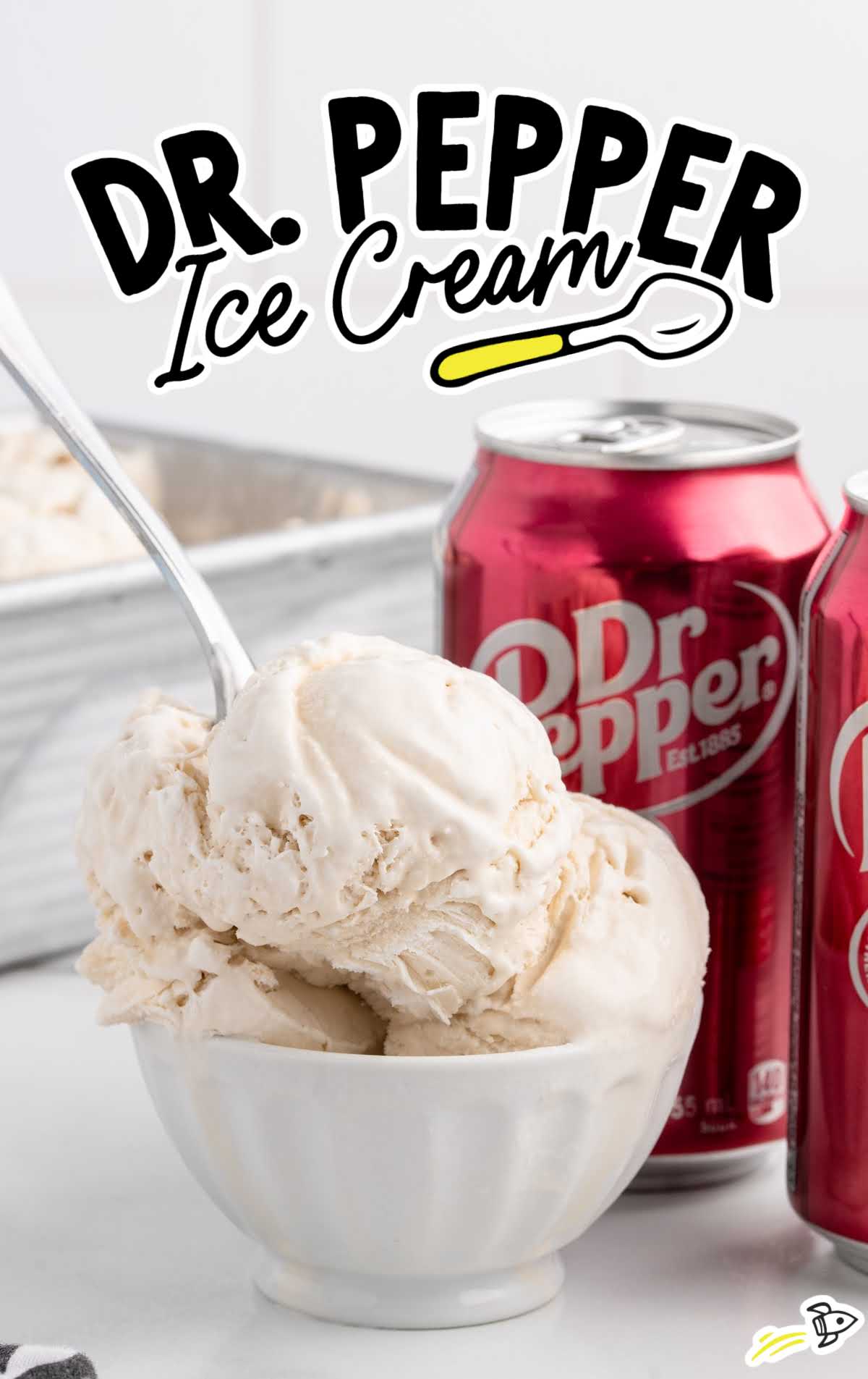 Large scoops of Dr Pepper ice cream in a white bowl with more scoops and Dr Pepper cans in the background