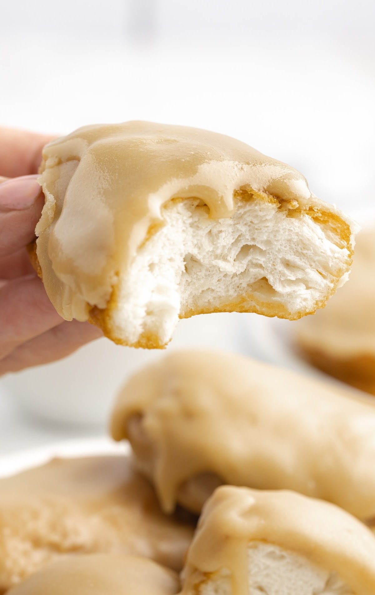 A hand is holding a maple bar with a bite out of it.