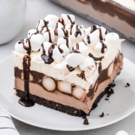 A slice of Hot Cocoa Lasagna is on a white dessert plate and drizzled with chocolate sauce.