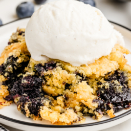 A serving of Lemon Blueberry Cobbler on a white plate with ice cream on top.