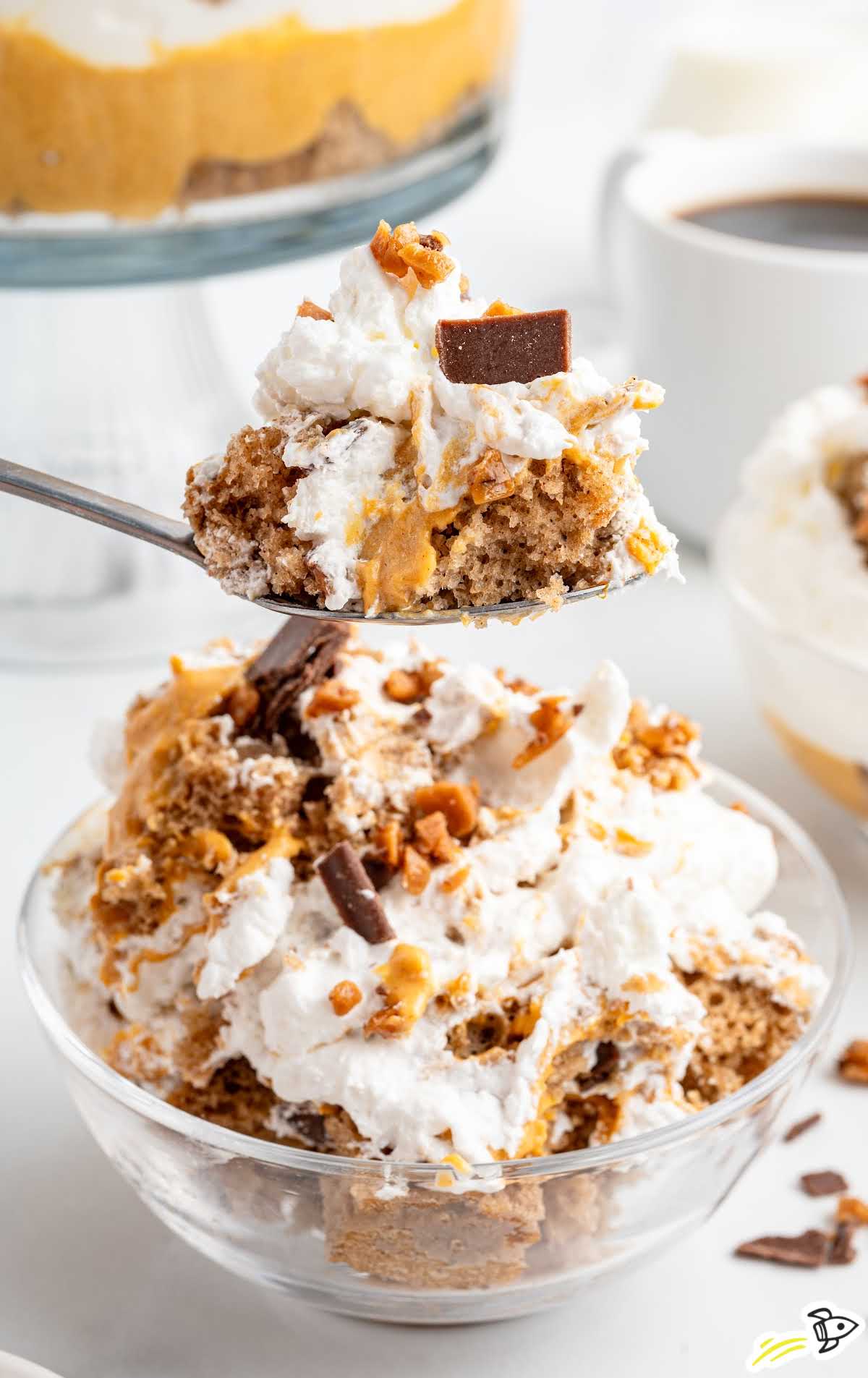 Spoonful of pumpkin trifle served in a small glass bowl with coffee in the background