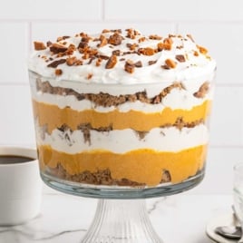 Pumpkin trifle dessert served in a trifle bowl with coffee cups and clear serving bowls beside it
