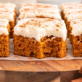 Squares of pumpkin bars with white frosting and a dusting of cinnamon on a wooden board.