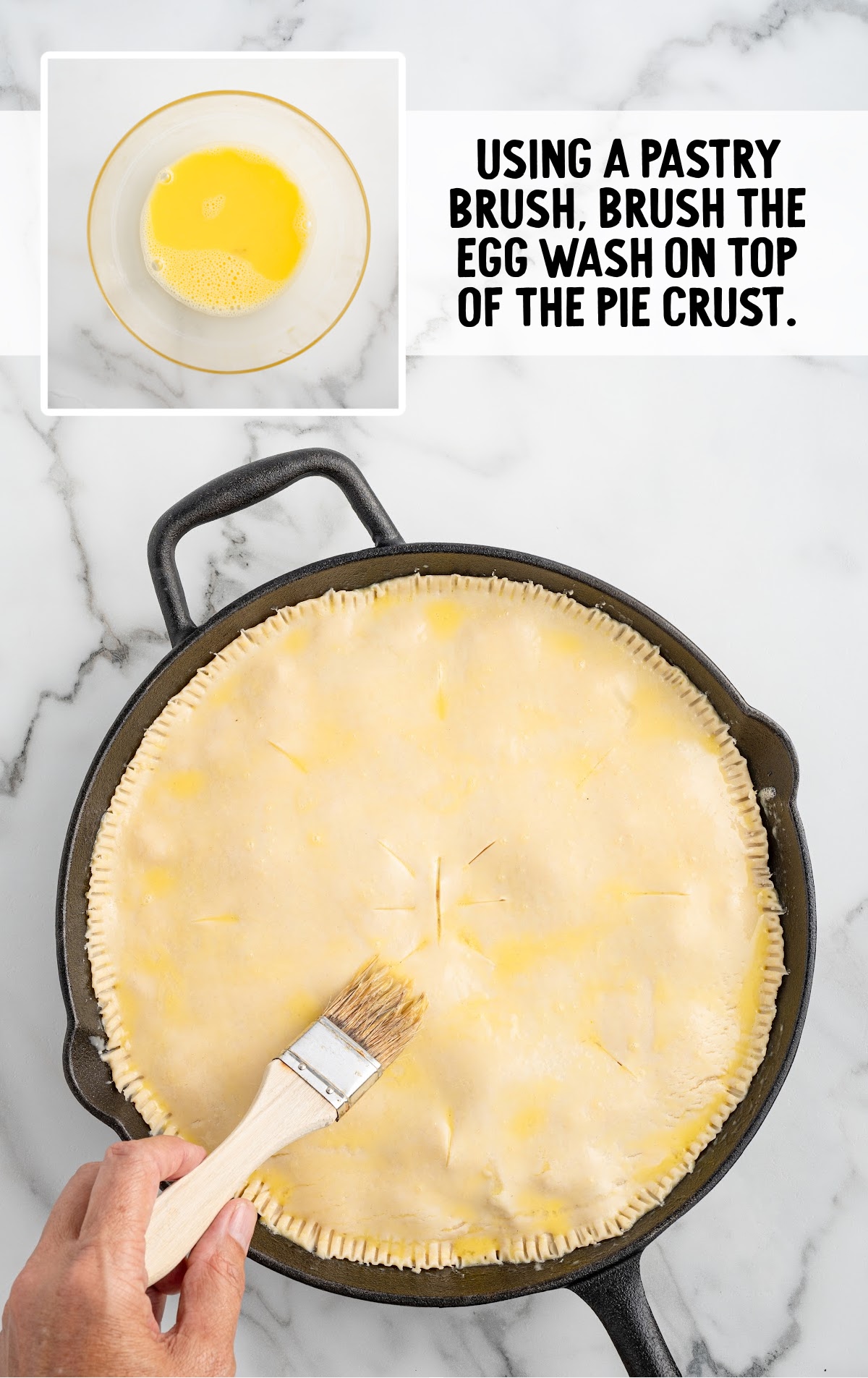 A person is brushing egg wash on top of the pie crust with a pastry brush.