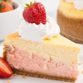 a slice of Strawberries and Cream Cheesecake topped with whipped topping and a strawberry on a plate