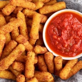 A bowl of marinara sauce sits next to a pile of crispy, golden-brown Stuffed Ziti Fritta on a tray lined with printed parchment paper.