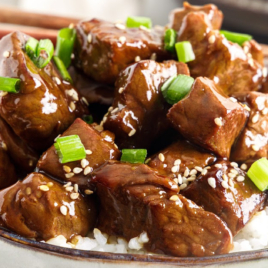 A bowl of rice topped with juicy and saucy teriyaki steak bites.