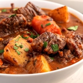 A close-up of a bowl of Beef Brisket Stew with chunks of tender beef, potatoes, carrots, and parsley in a rich, brown broth.