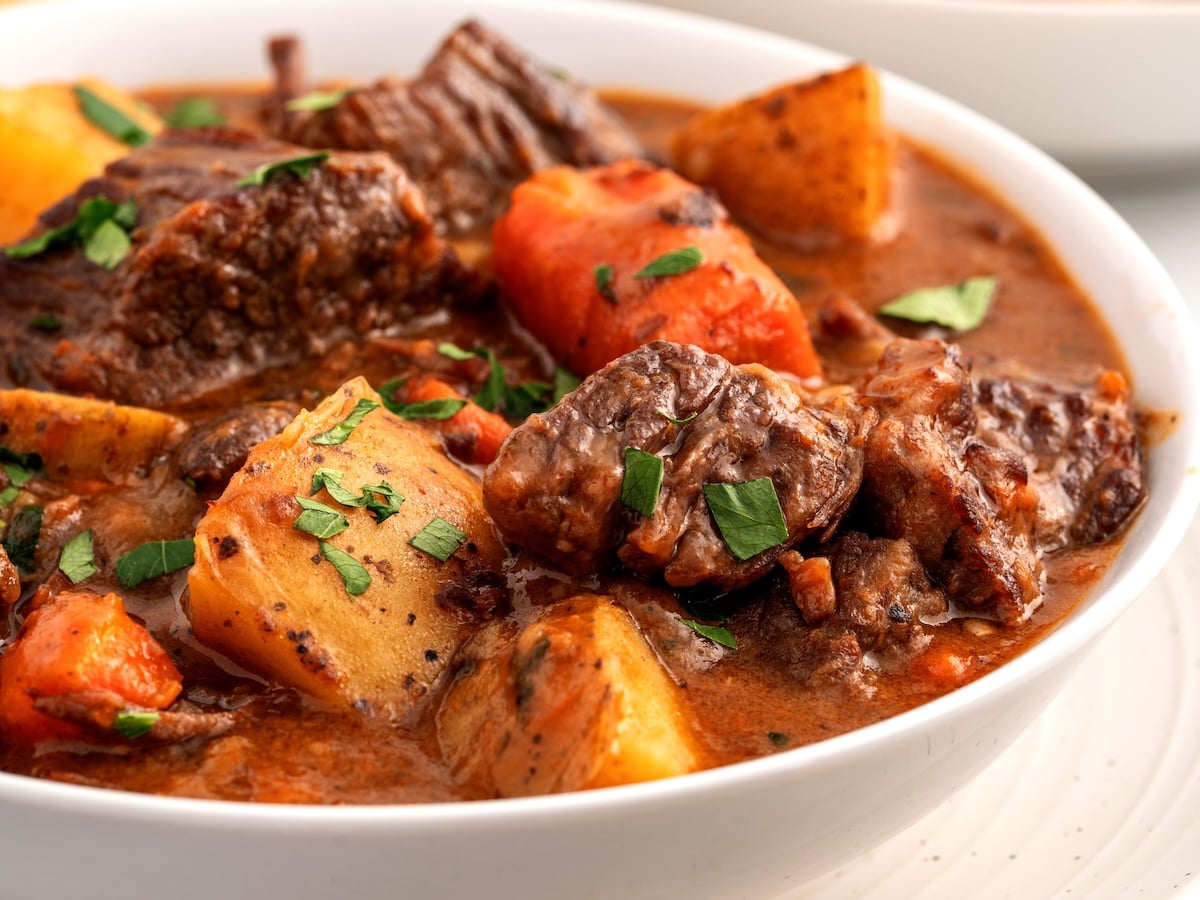 A close-up of a bowl of Beef Brisket Stew with chunks of tender beef, potatoes, carrots, and parsley in a rich, brown broth.